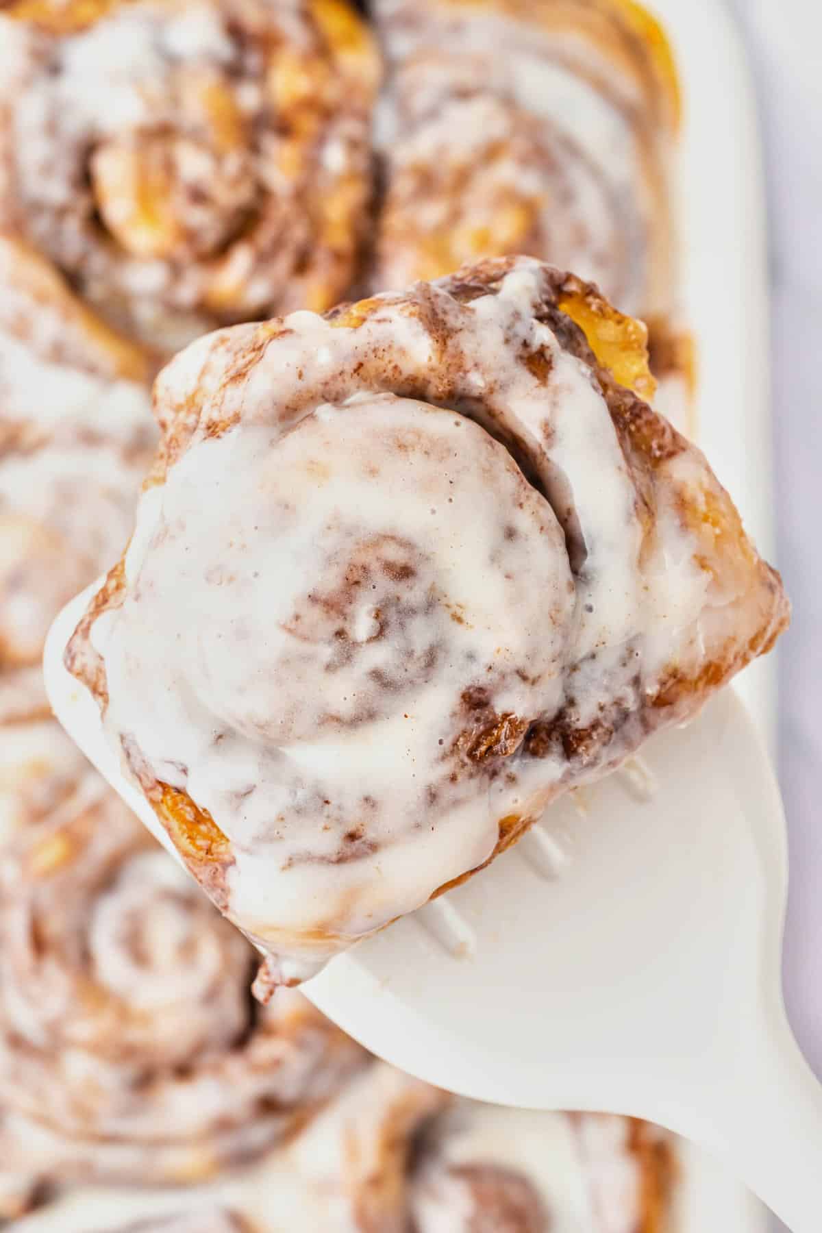 A spatula lifting up a cinnamon roll out of a pan.