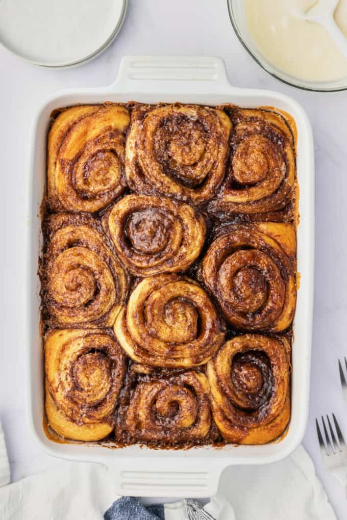 Baked cinnamon rolls in a white dish before being frosted  with cinnamon roll frosting.