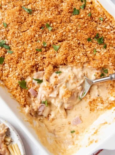 A chicken casserole with part of it scooped out showing a creamy sauce under crispy breadcrumb topping.