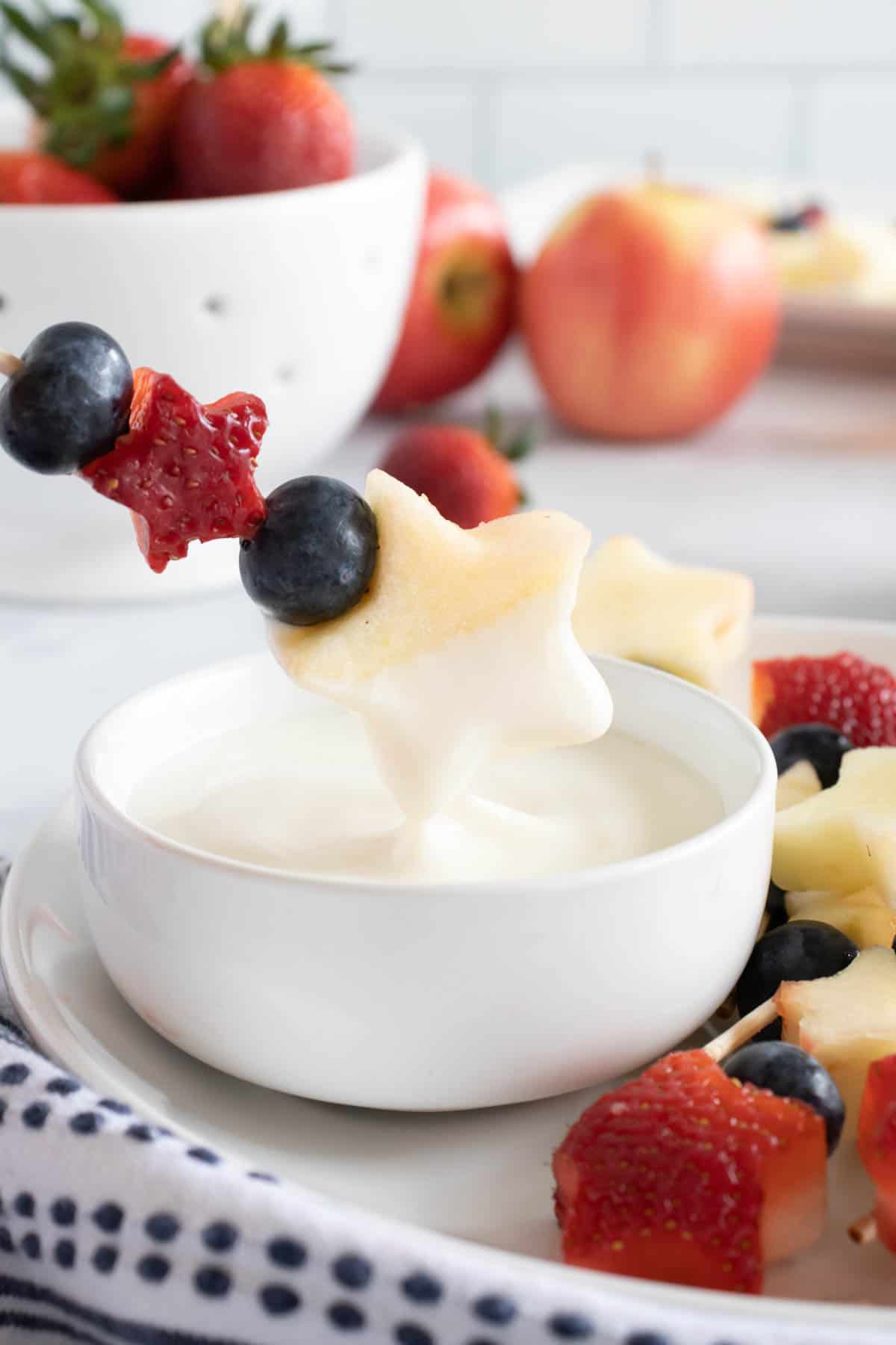 A 4th of July patriotic fruit kabob being dipped into a homemade yogurt dipping sauce.