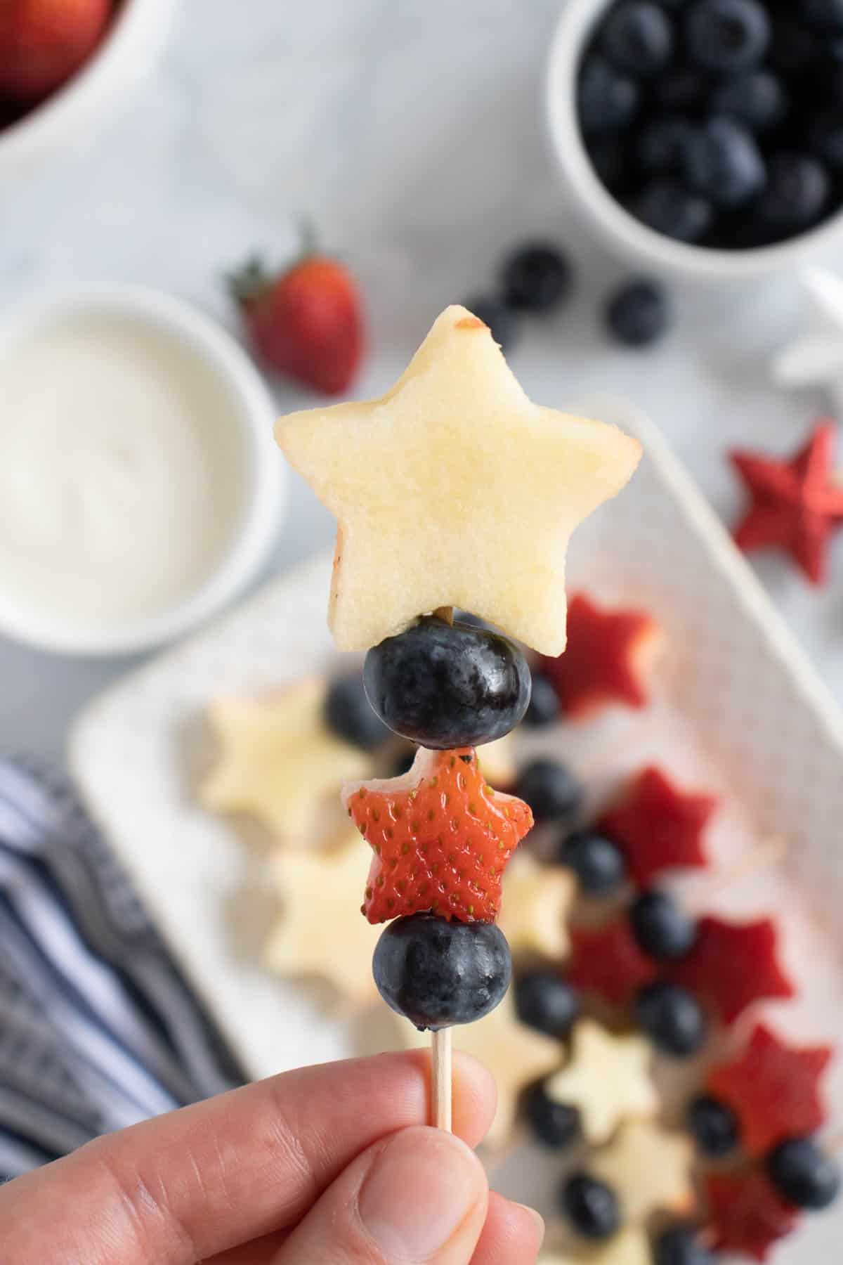 A patriotic fruit kabob made with strawberries, blueberries, and apples held over a yogurt dip.
