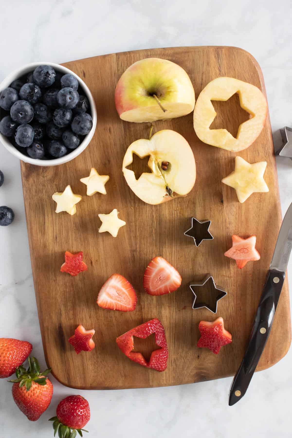 Cutting apple and strawberry slices into straws on a wooden cutting board.