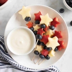 Fourth of July fruit Kabobs on a plate with a bowl of yogurt fruit dip.