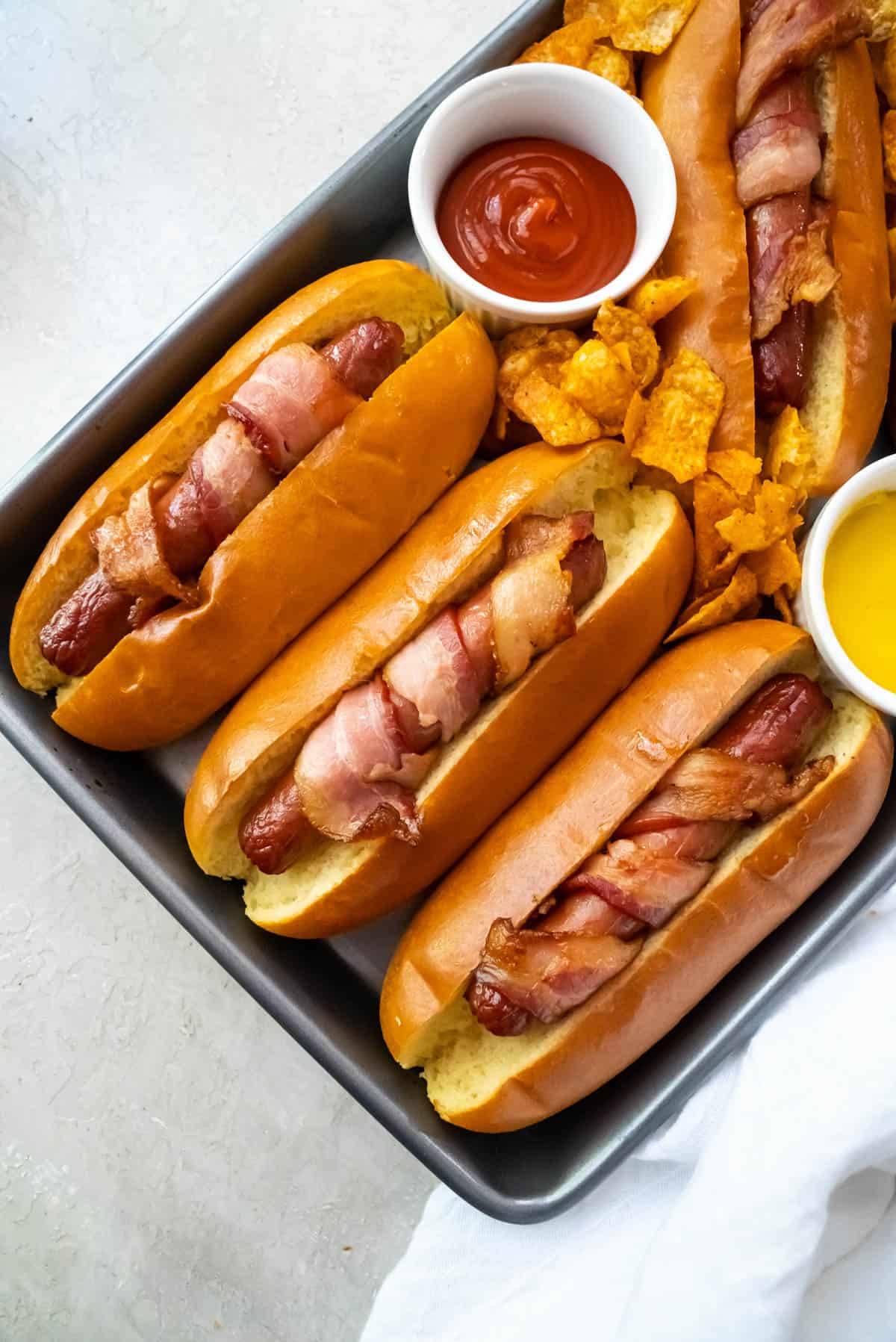 An overhead image of three bacon wrapped hot dogs in buns.