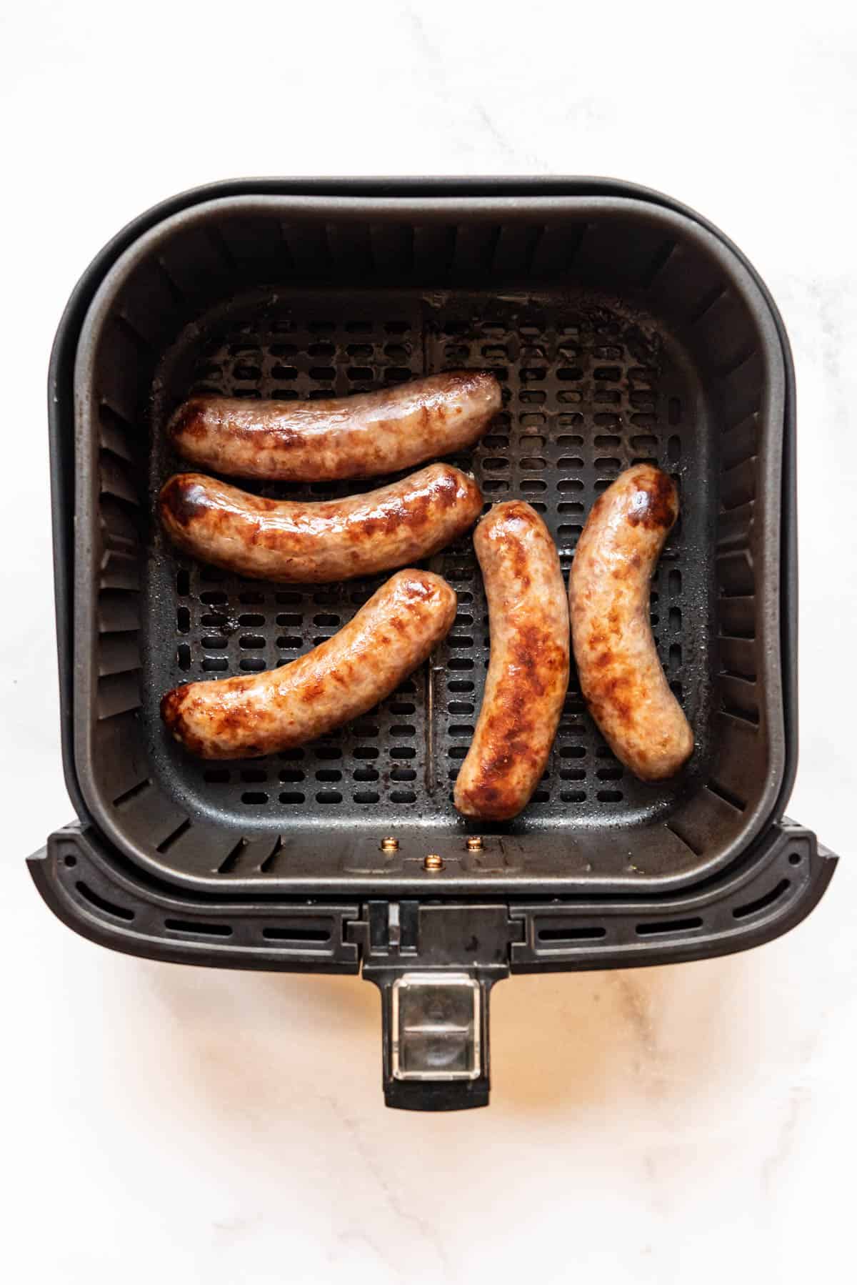 Top view of a square air fryer basket with cooked brats in it.
