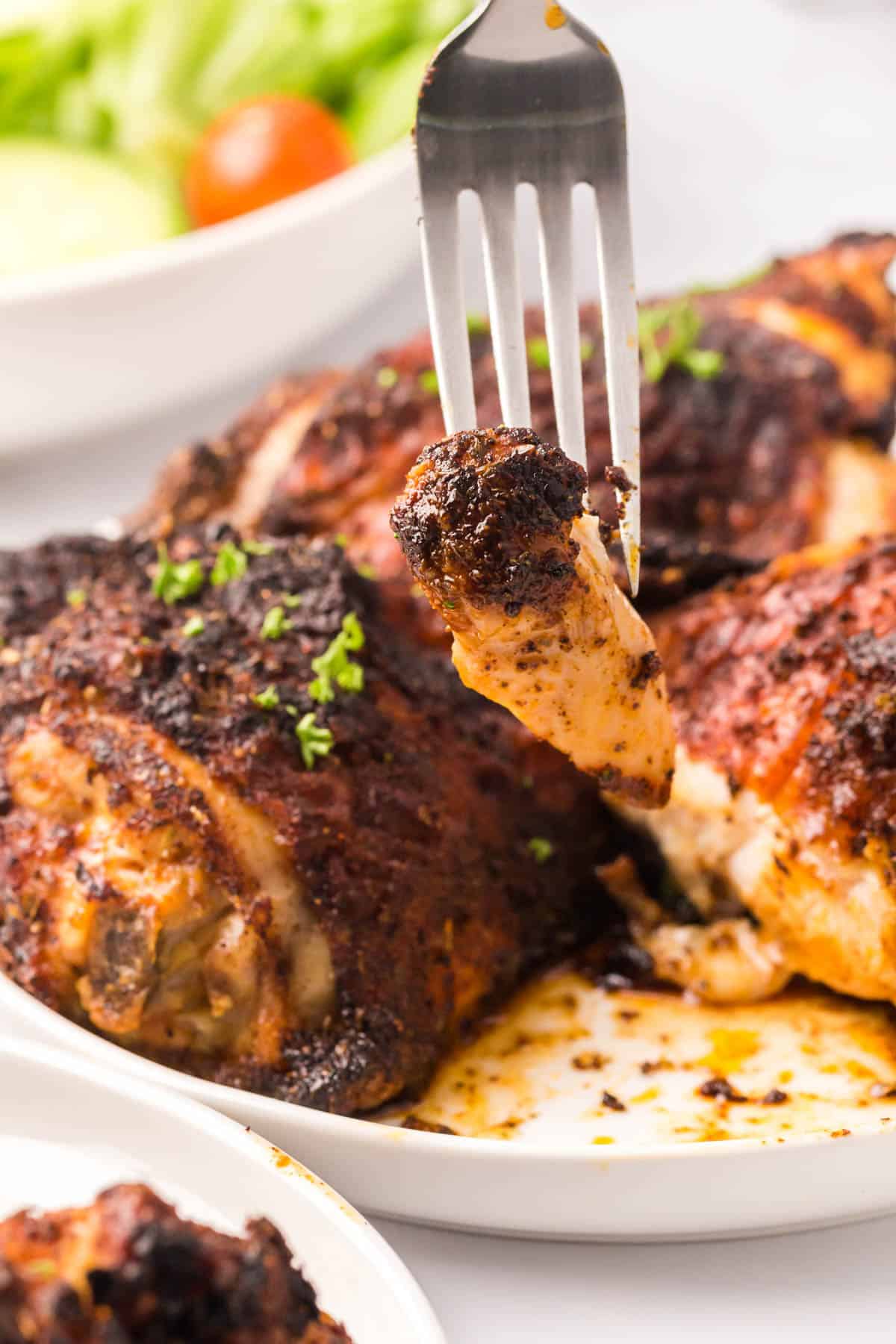 Close up of blackened chicken thighs on a white plate being pierced with a fork.