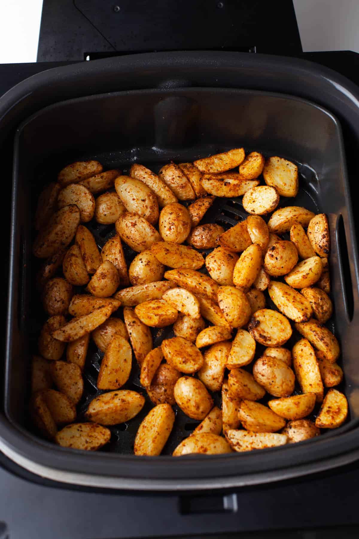 Top view of air fryer basket with chopped and seasoned potatoes in it. 