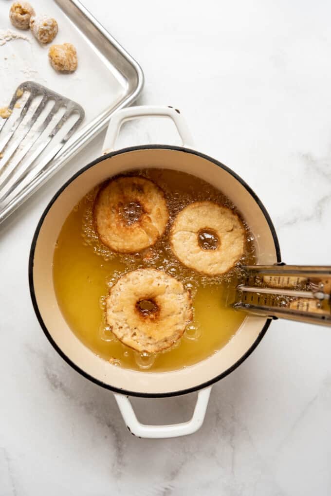 Three apple cider donuts frying in hot oil.