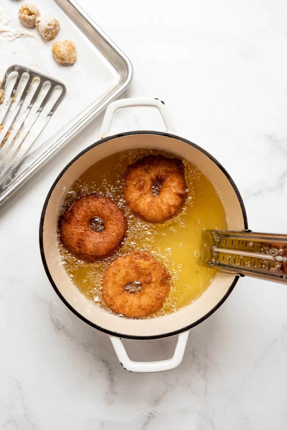 Three apple cider donuts frying until golden brown in hot oil in a dutch oven.