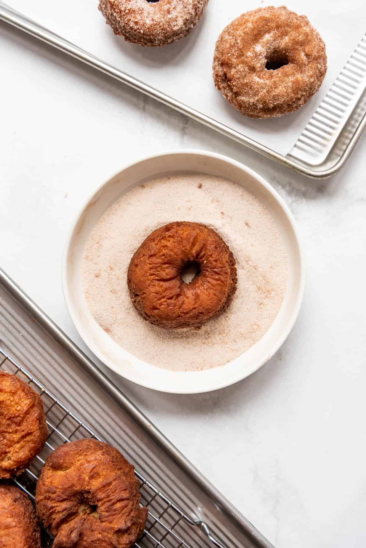 Dipping freshly fried donuts into a cinnamon sugar mixture in a shallow bowl.