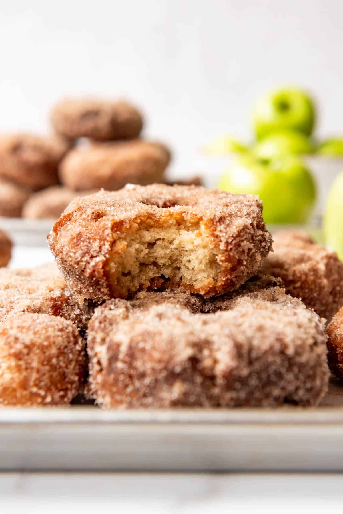 An apple cider donut with a bite taken out of it sitting on top of more donuts.