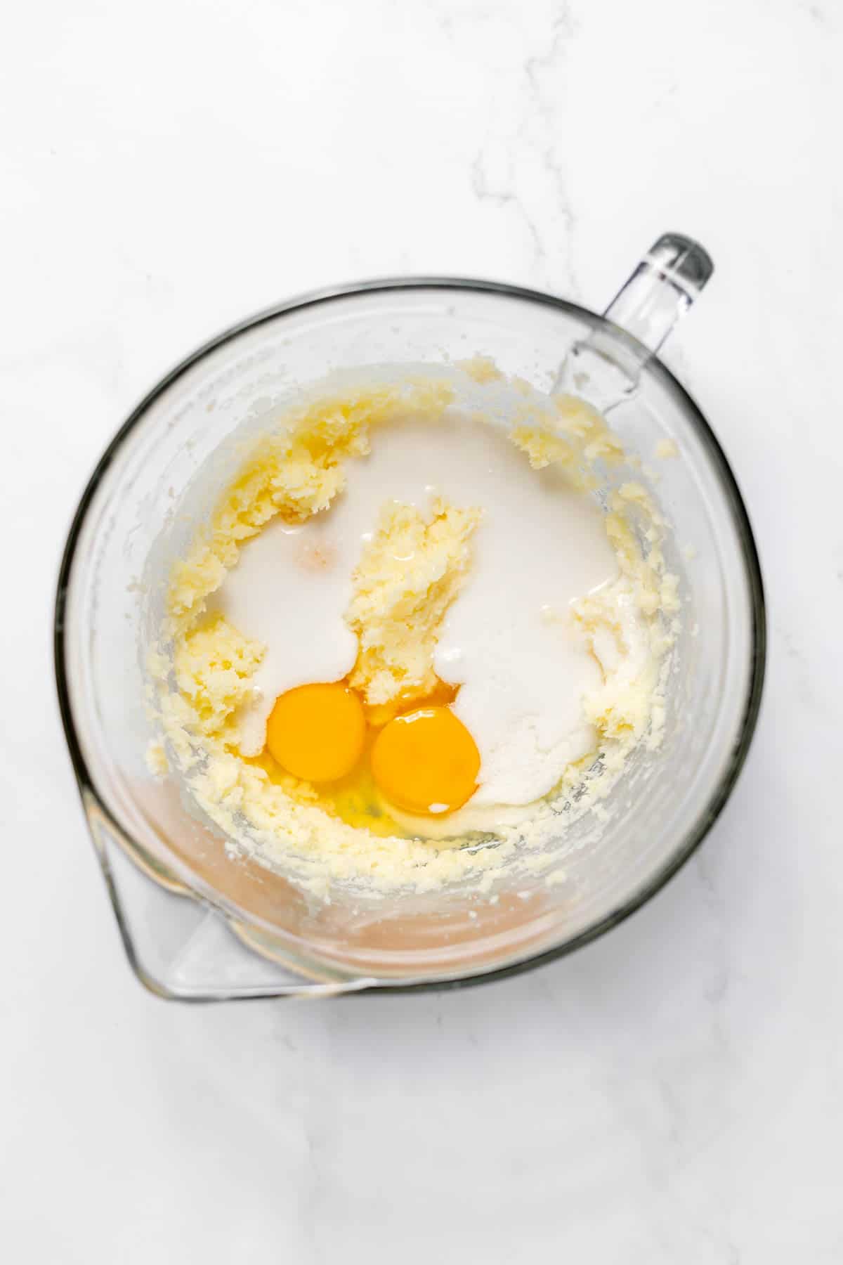 Top of a large glass mixing bowl with creamed butter and sugar in the bottom, and egg and milk on top. 