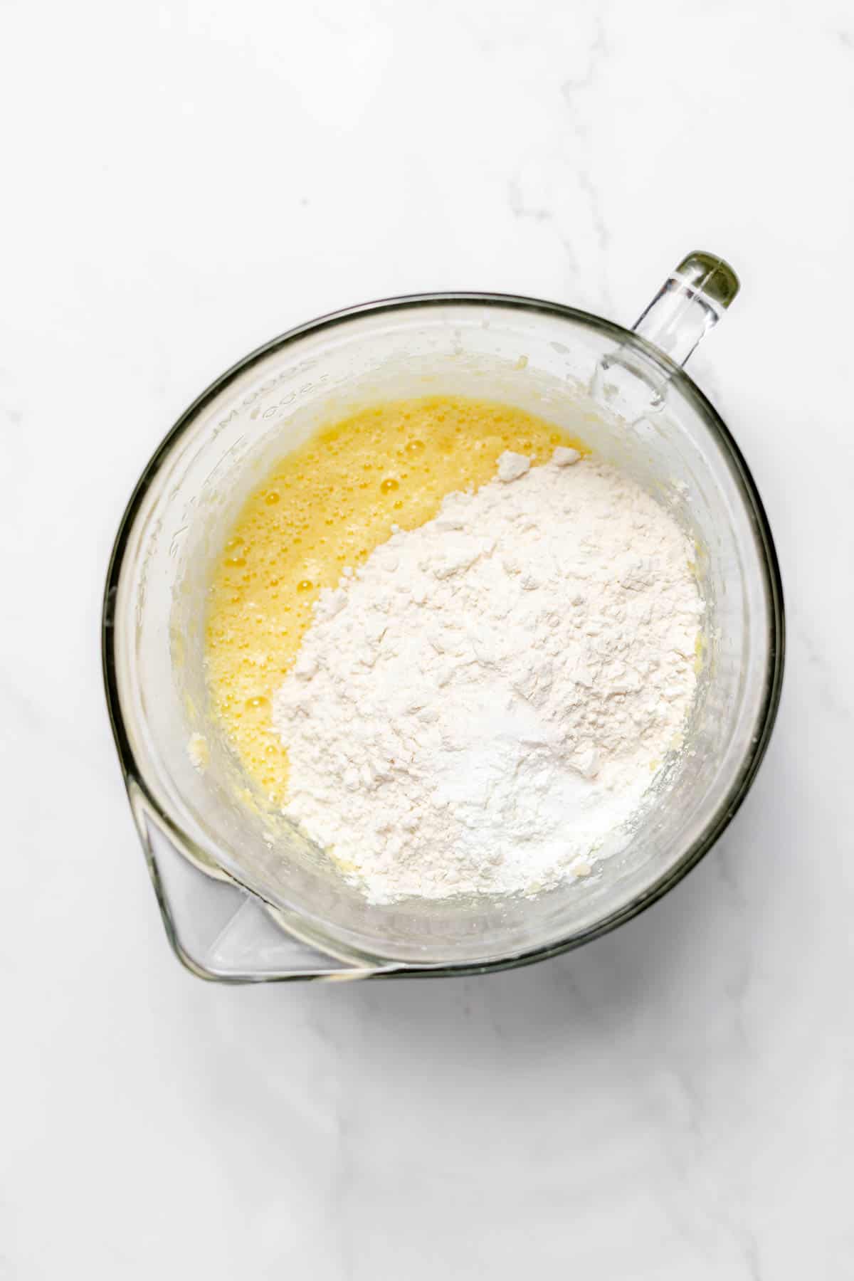 Top view of a glass mixing bowl with a creamed mixture in it, and a flour mixture on top. 