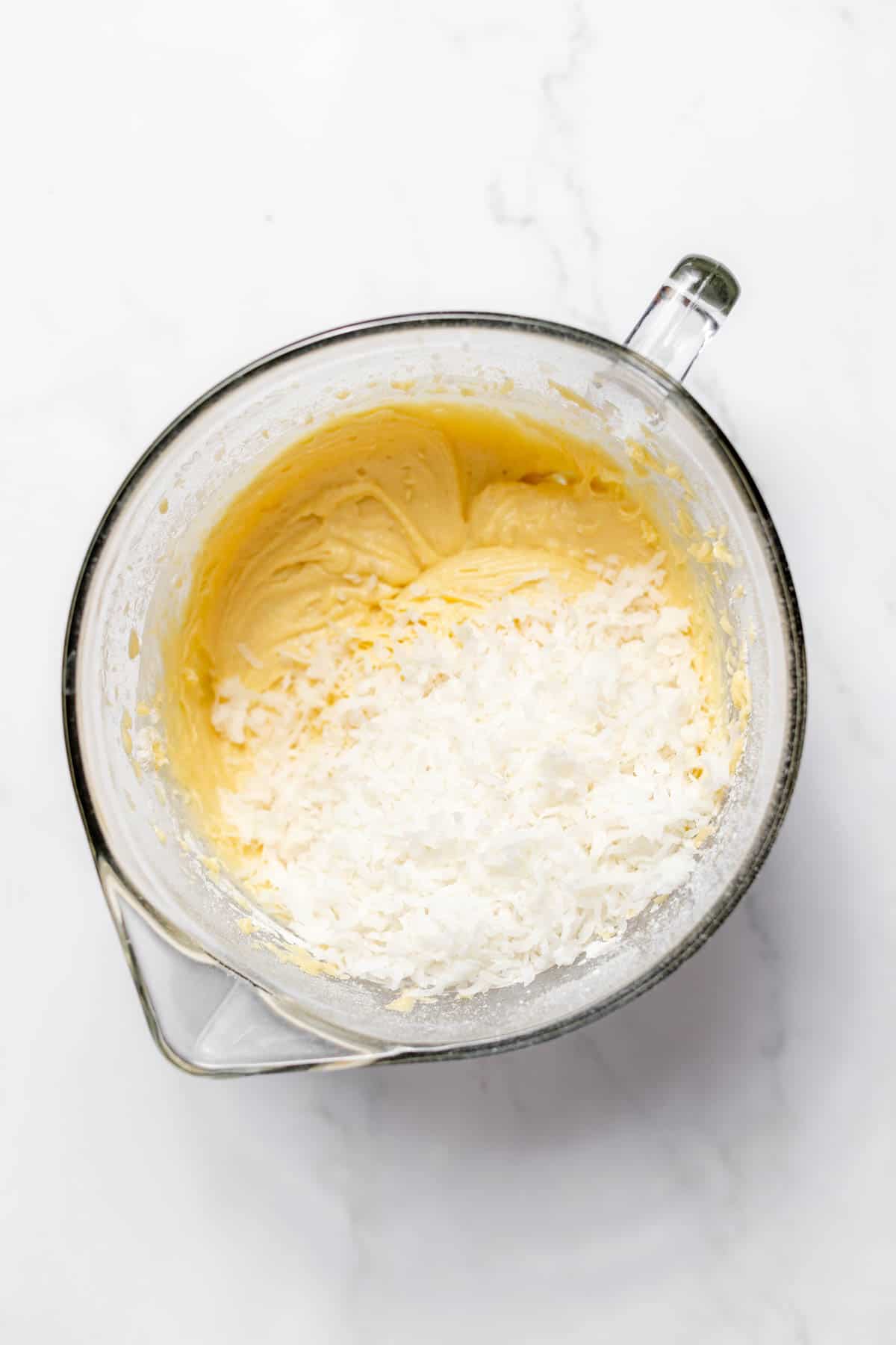 Top view of a glass mixing bowl with a thickened creamed mixture in it, and a flour mixture on top. 
