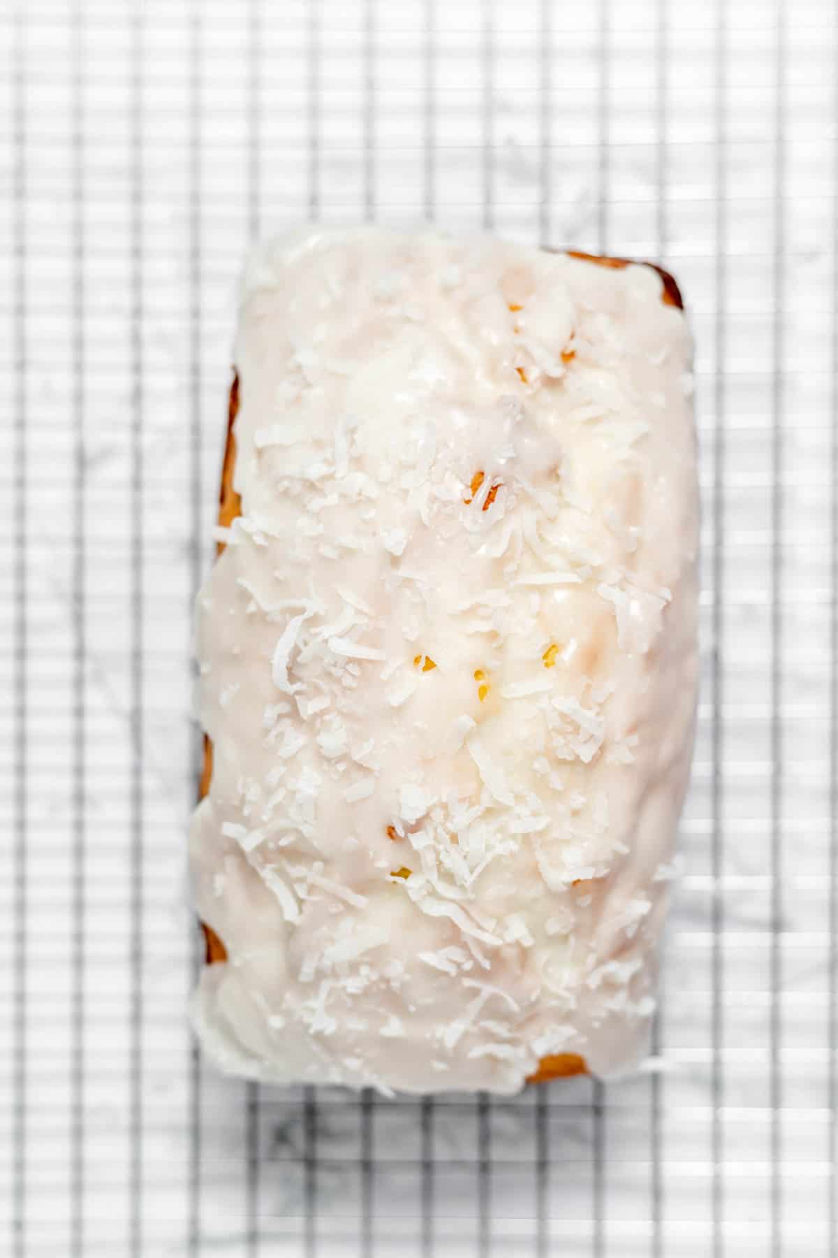 Top view of a baked Coconut bread loaf on a wire rack with a white glaze on top. 