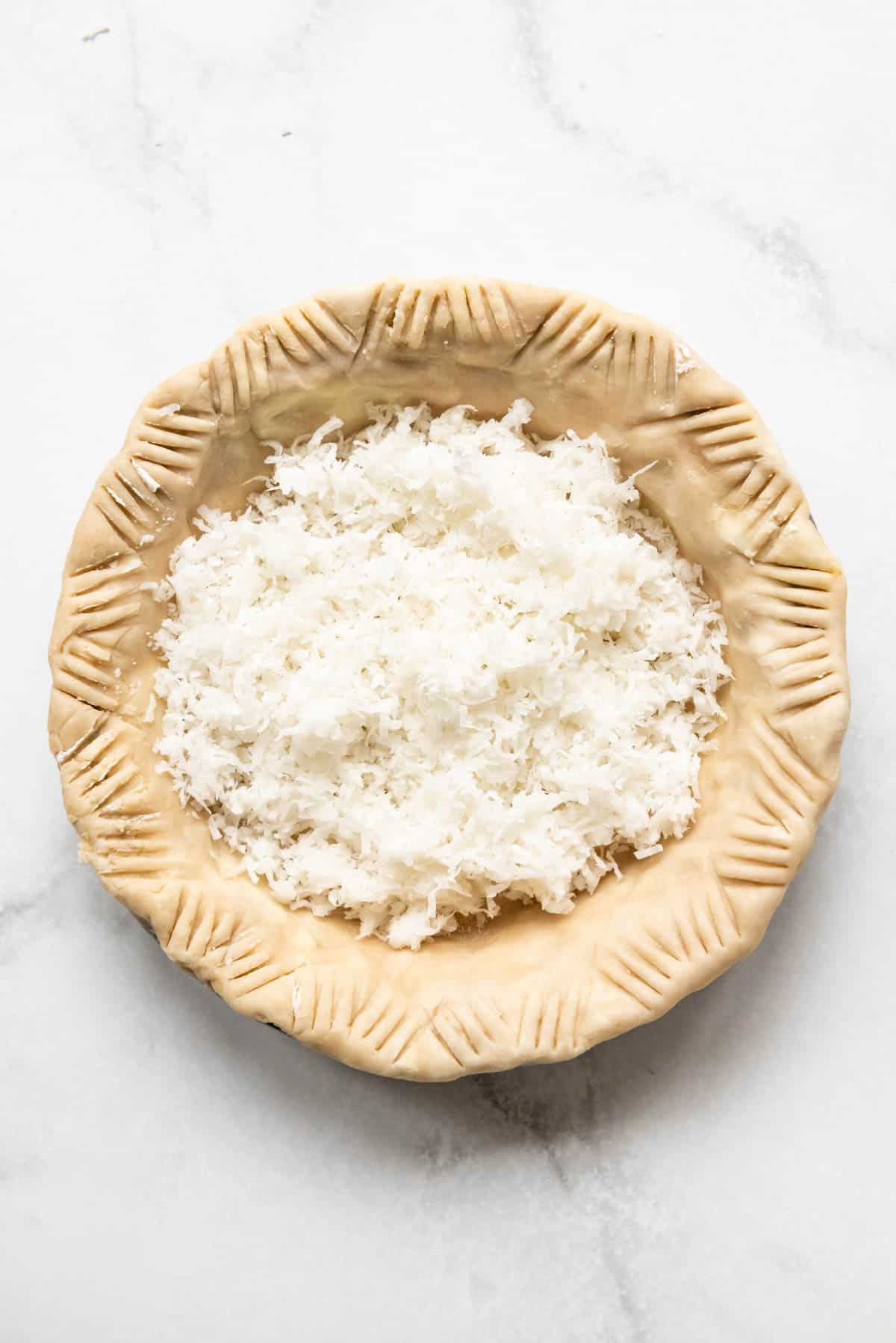 An unbaked pie crust filled with shredded sweetened coconut.