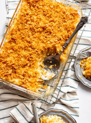A serving spoon in a baking dish of funeral potatoes.