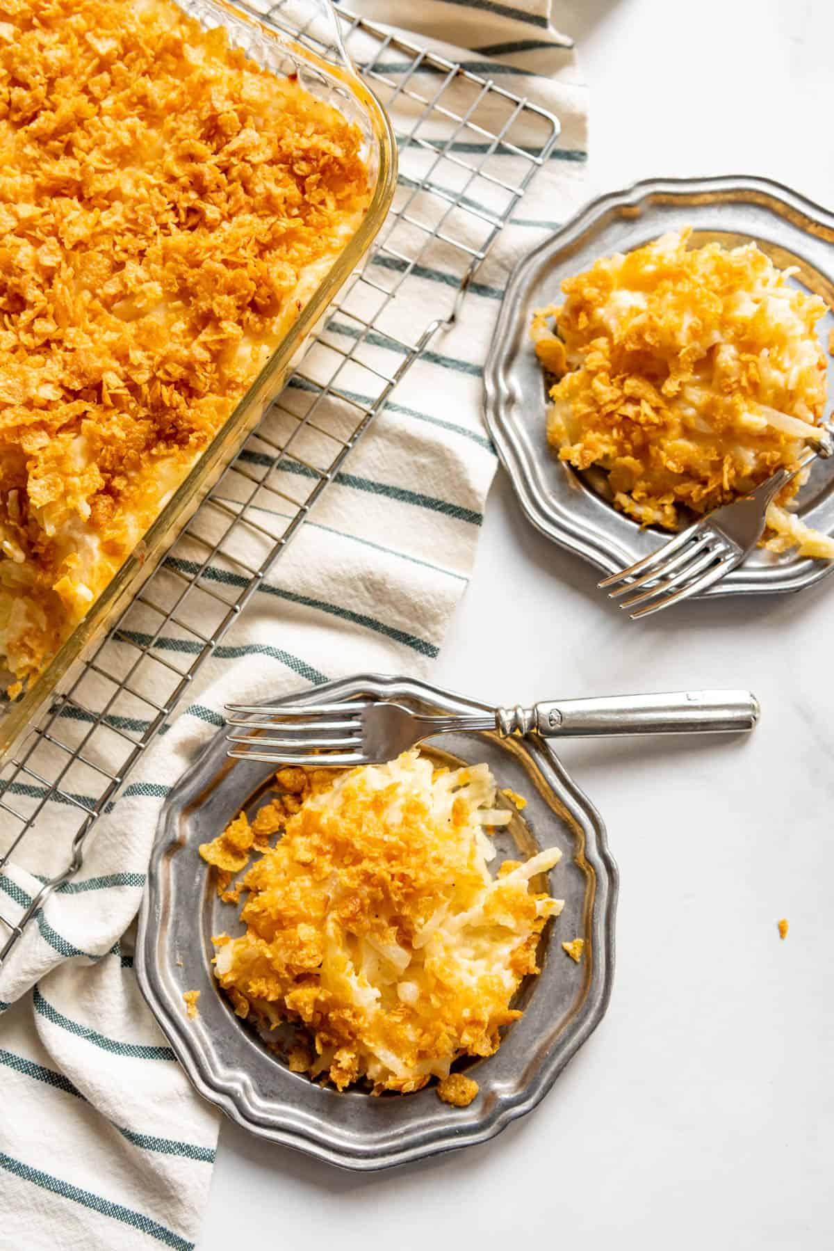 Plates of cheesy funeral potatoes next to a casserole dish.