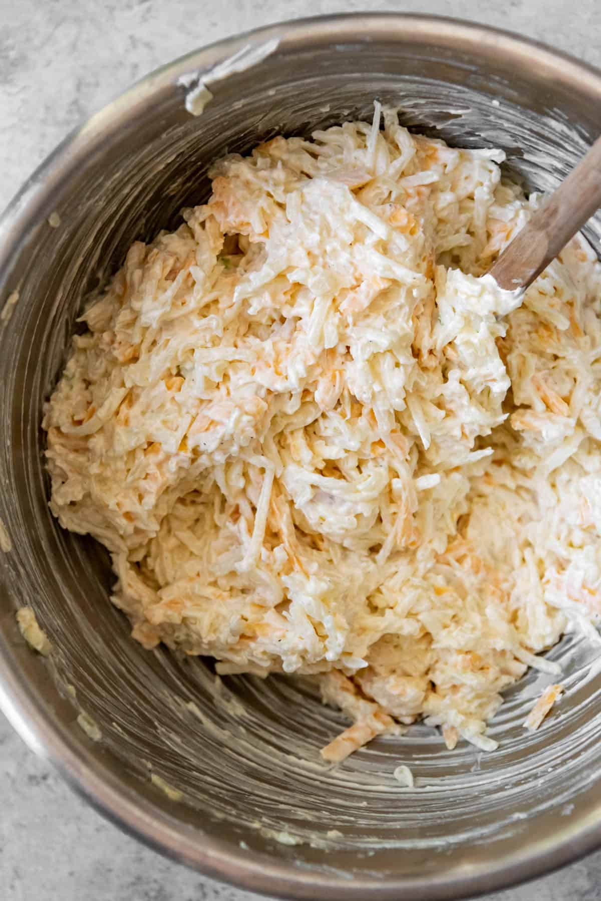 Mixing frozen hashbrowns with sour cream and cheese for funeral potatoes.