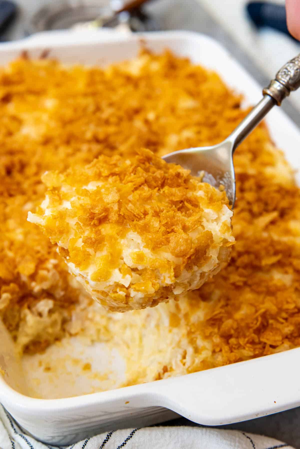 A serving spoon lifting a big scoop of funeral potatoes from the pan.