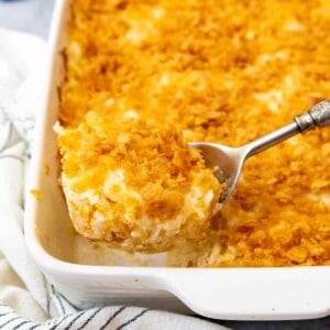 A serving spoon lifting a big scoop of funeral potatoes from the pan.