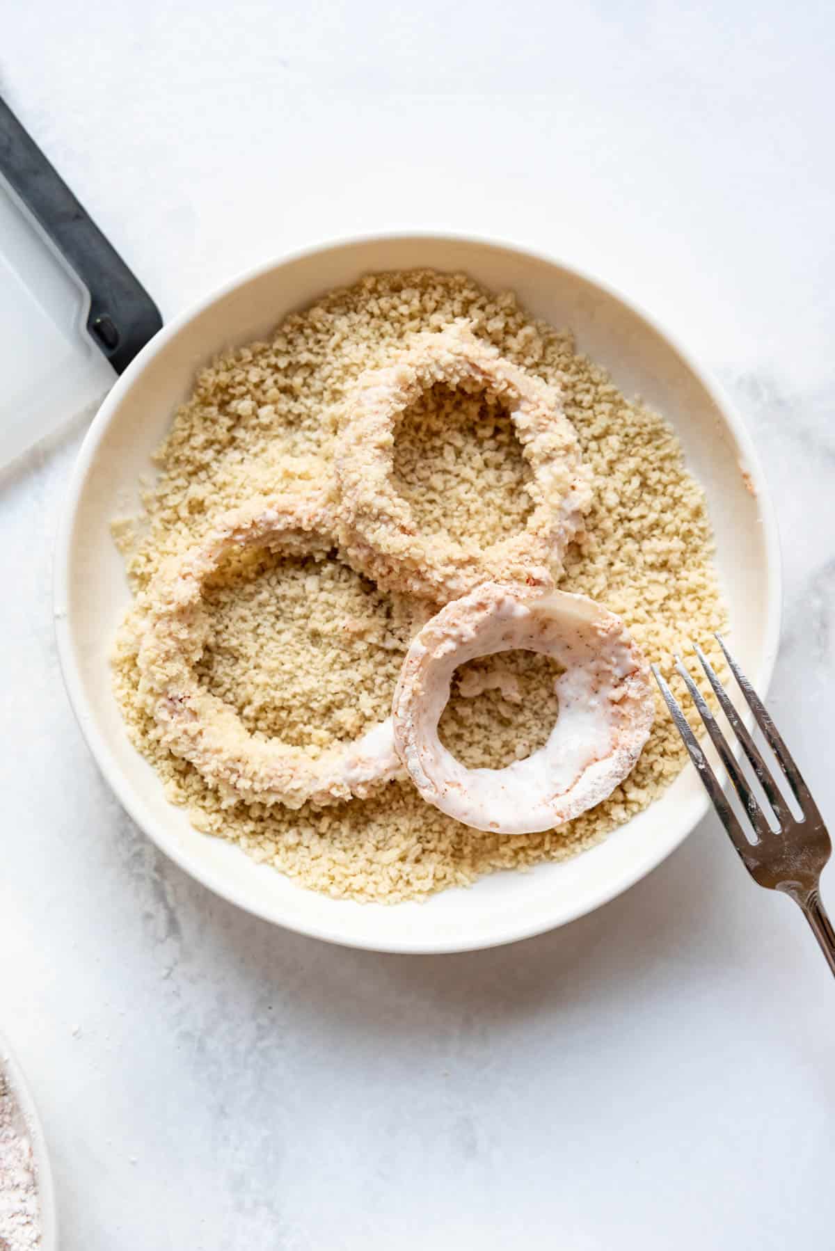 Breading onion rings in a breadcrumb coating before frying.