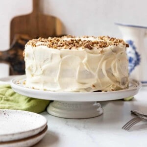 A frosted hummingbird cake on a white cake stand.