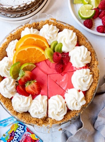 A sliced Kool-Aid pie decorated with whipped cream and fresh orange and lime slices.