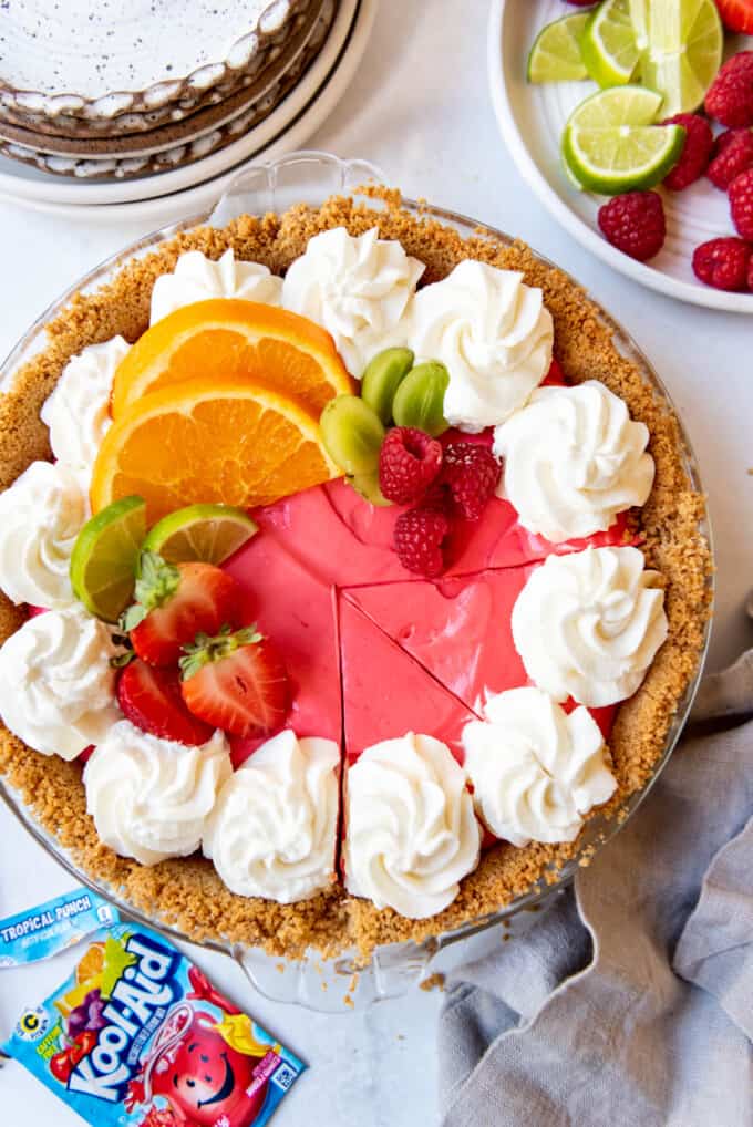 A sliced Kool-Aid pie decorated with whipped cream and fresh orange and lime slices.