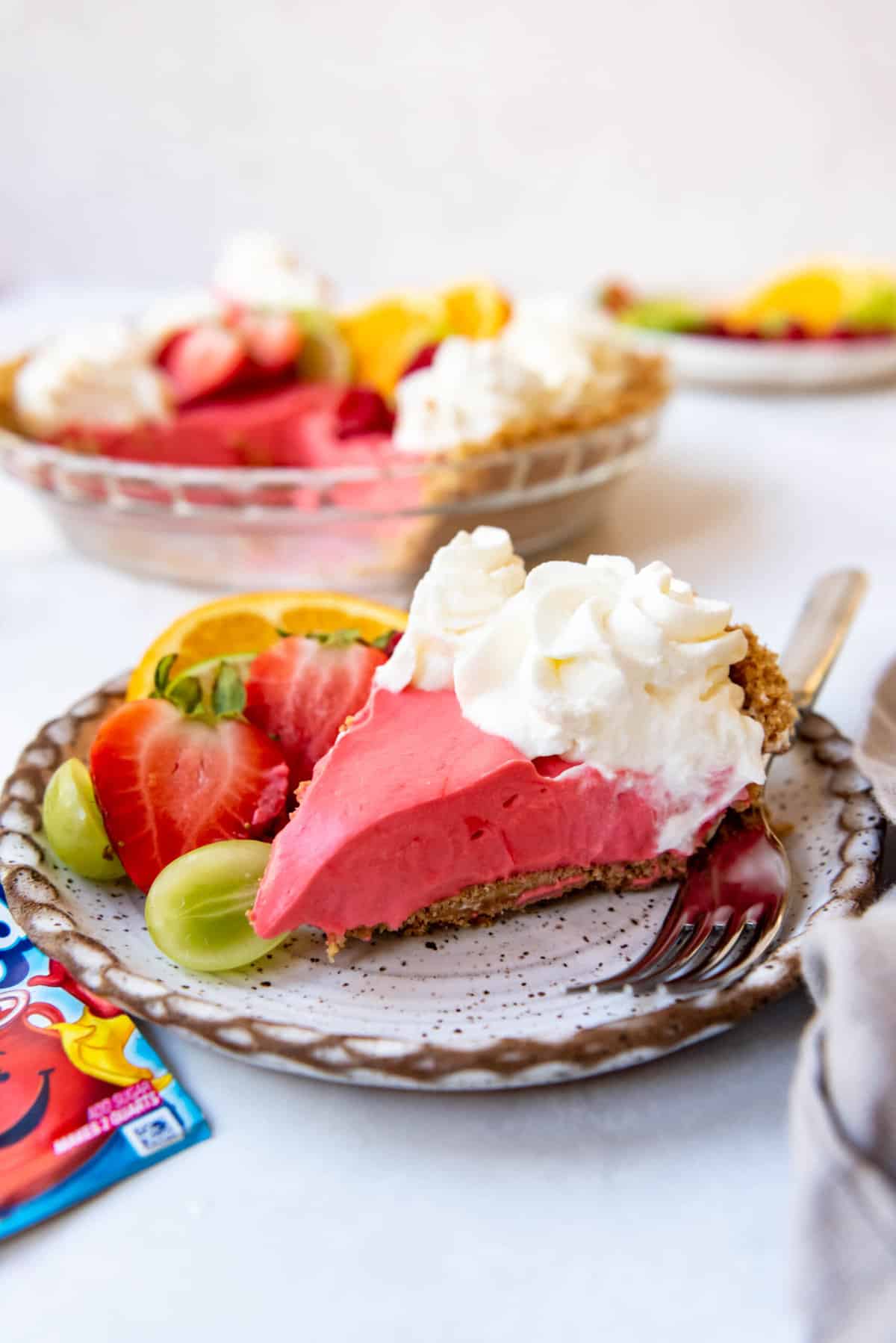 A slice of Kool-Aid pie on a plate with fresh fruit.