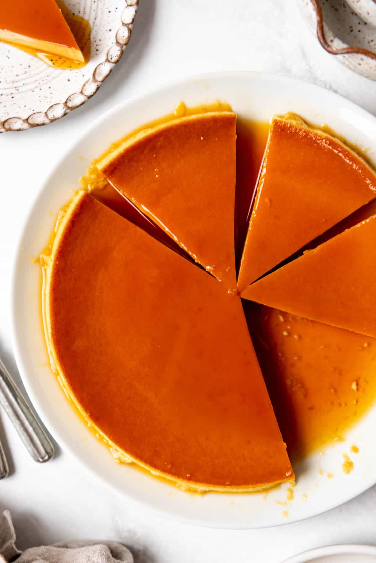 Top view of Mexican Flan on a white plate on a white table, with slices cut out of it. 