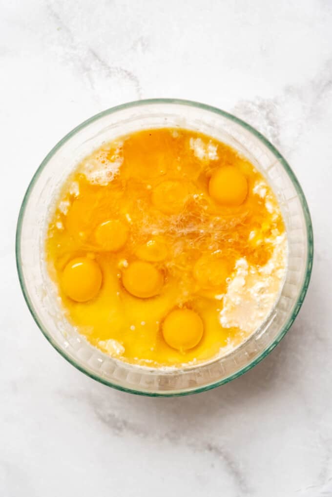 Top view of a glass mixing bowl with milk, eggs, vanilla, and orange zest in it.