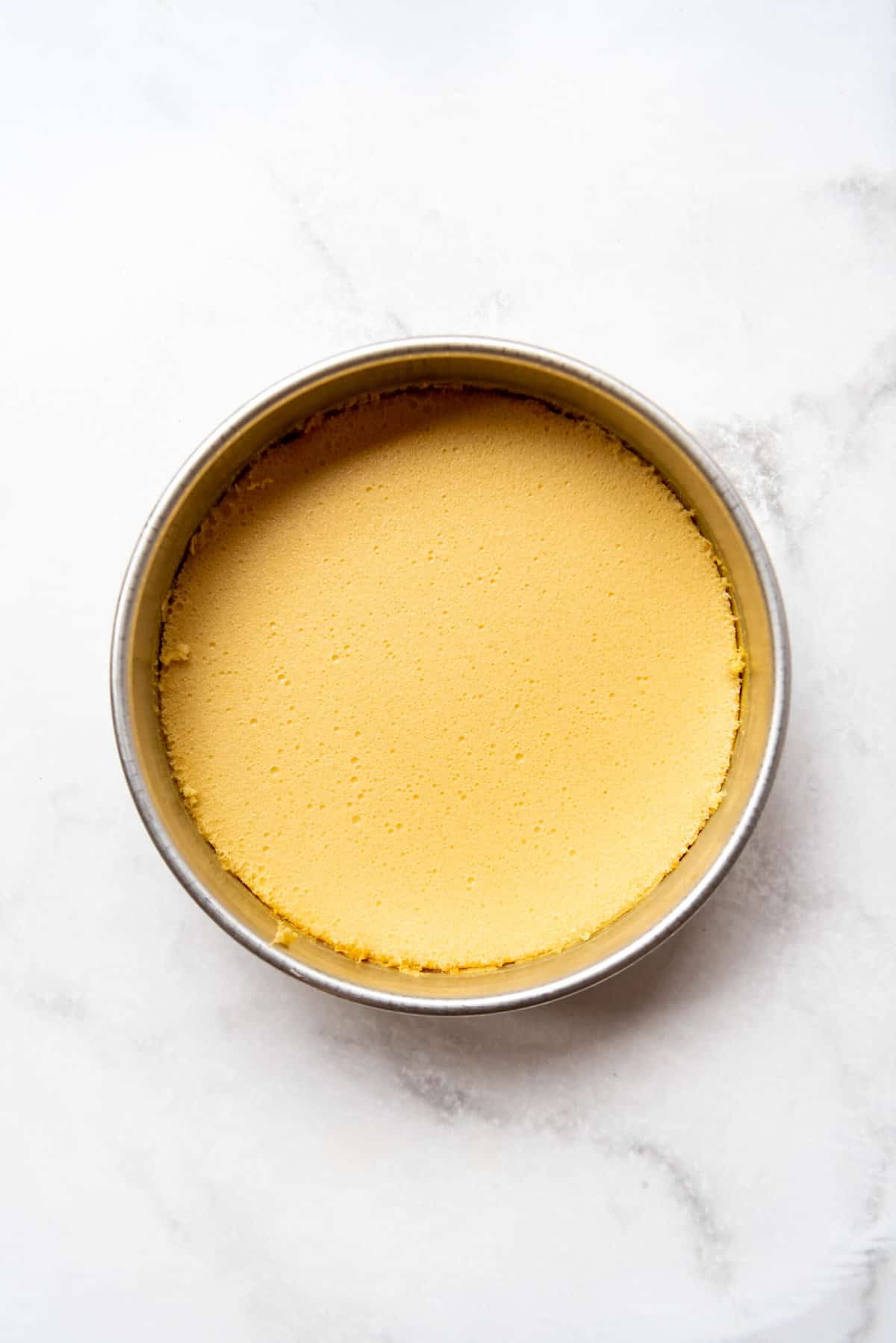 Top view of flan mold in a water bath and a yellow mixture on the top. 