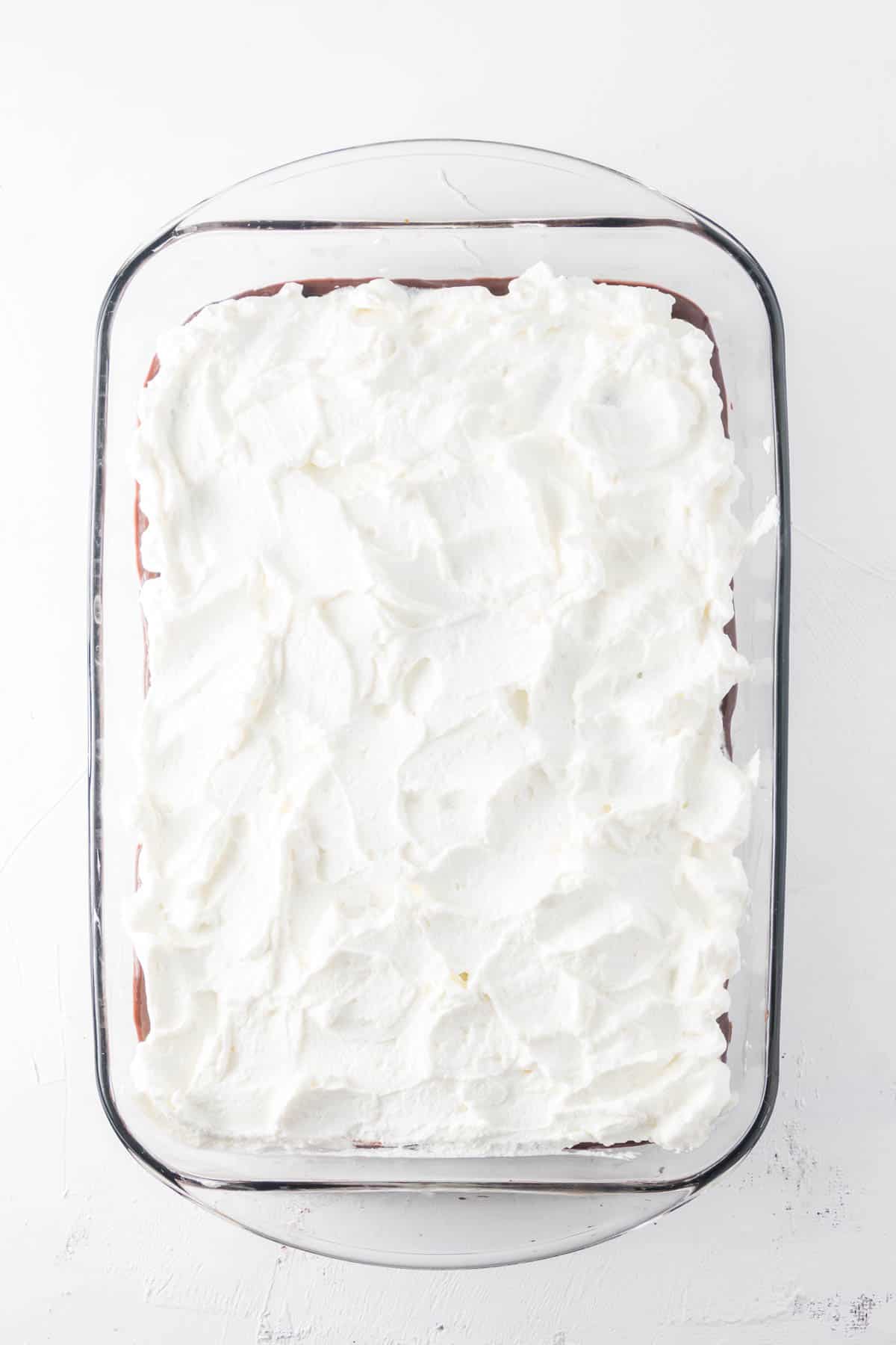 Topping a chocolate pudding layer with sweetened whipped cream.