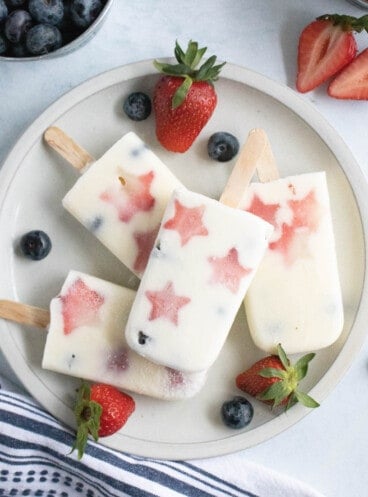 A plate of patriotic popsicles next to strawberries and blueberries.