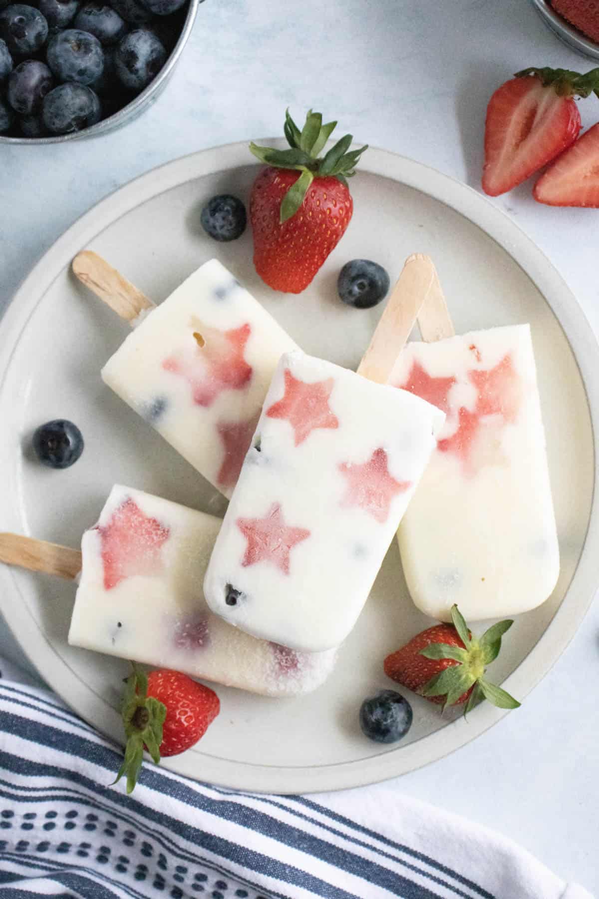 A plate of patriotic popsicles next to strawberries and blueberries.