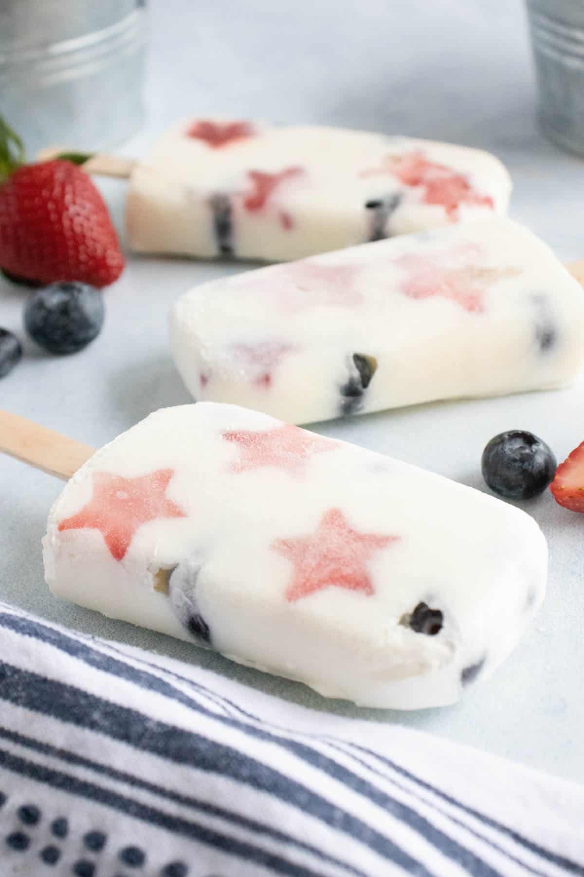 A side angle o f patriotic fruit and yogurt popsicles next to a striped blue and white cloth napkin.