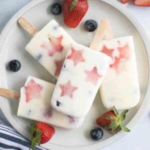 Patriotic popsicles on a plate with strawberries and blueberries.