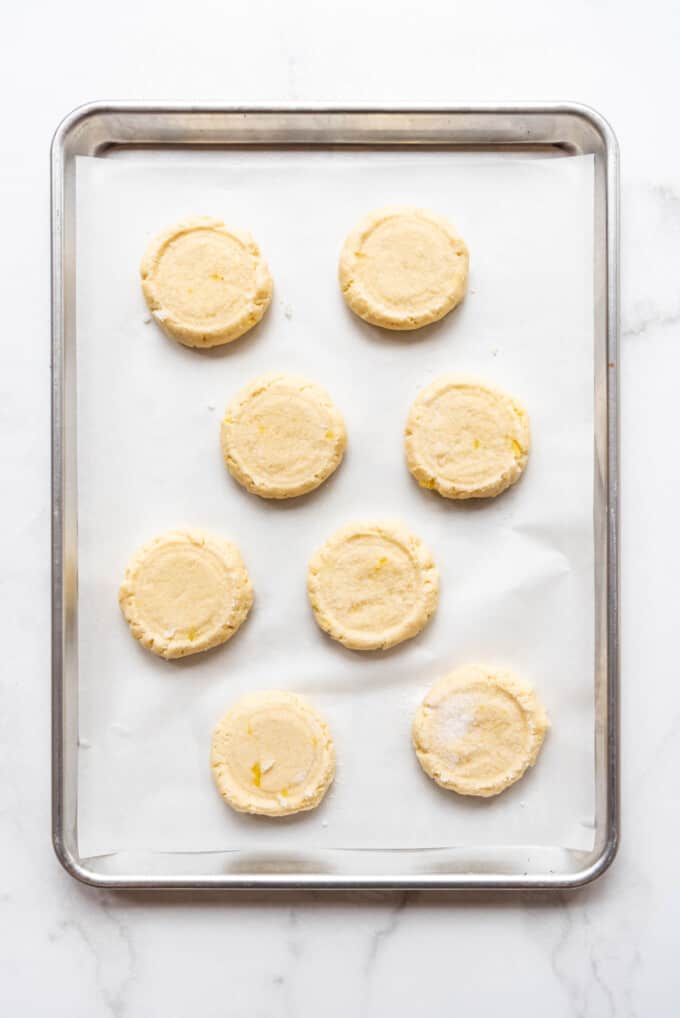 Pineapple coconut sugar cookies pressed flat on a baking sheet lined with parchment paper.
