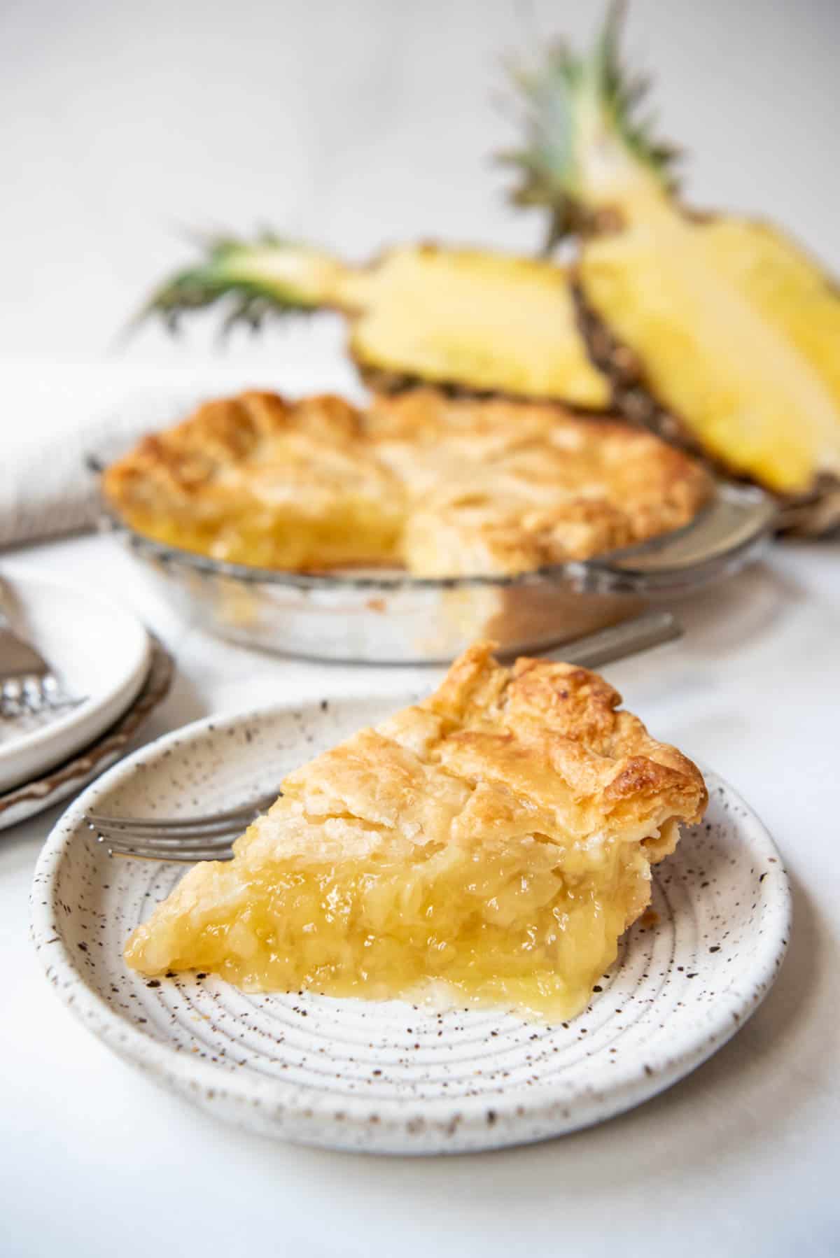 A slice of pineapple pie on a plate in front of the rest of the pie.