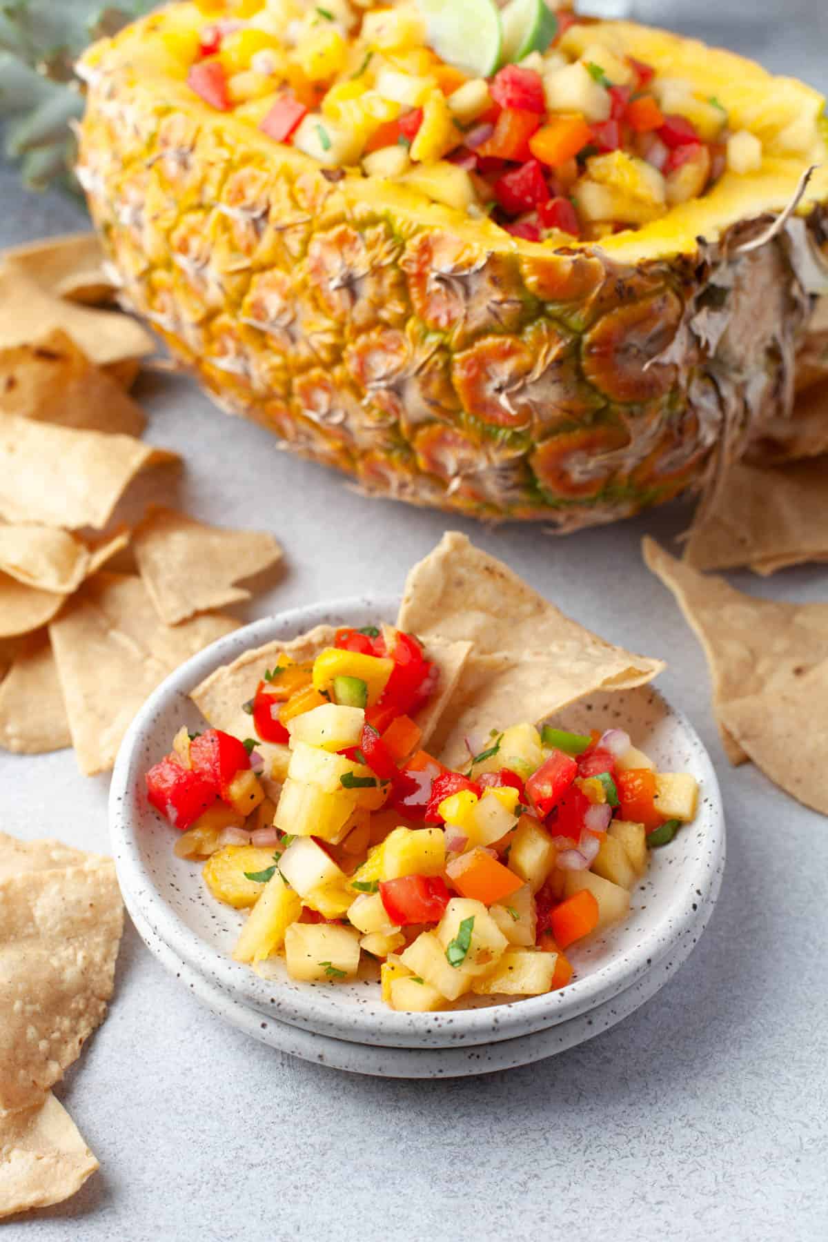 Pineapple salsa on a small plate in front of a half pineapple filled with pineapple salsa.