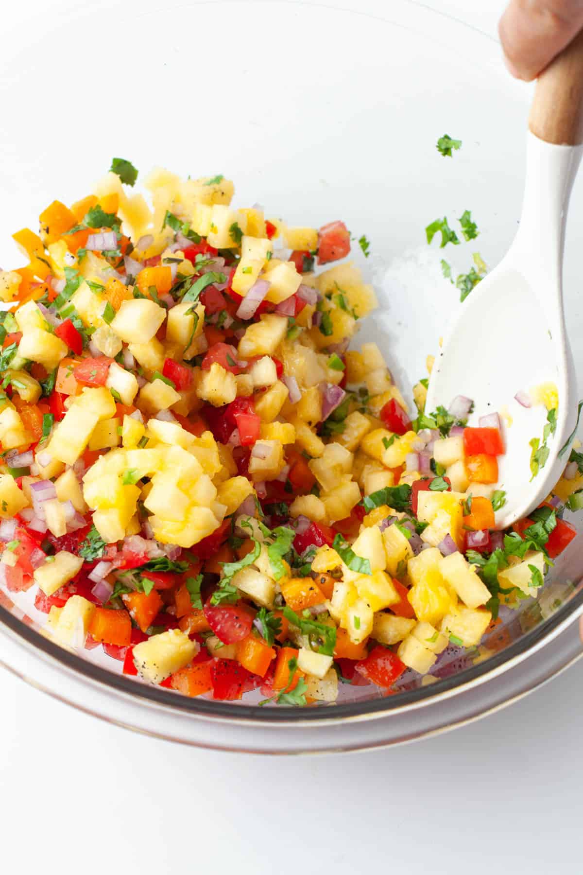 A spoon stirring pineapple salsa ingredients together in a large glass bowl.