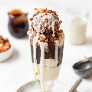 A tin roof sundae in front of jars of chocolate sauce and marshmallow sauce.