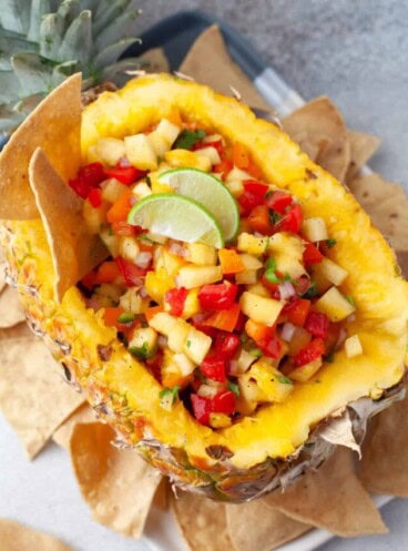 Pineapple salsa in a hollowed out pineapple with corn tortilla chips around it.