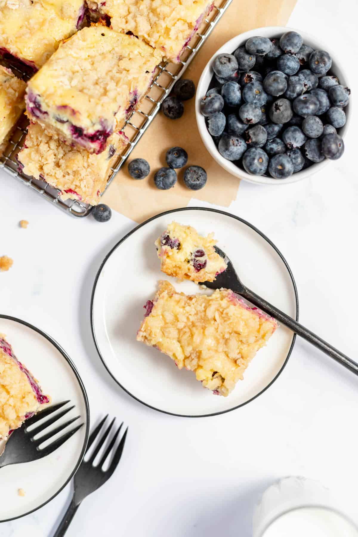 An overhead image of a blueberry cheesecake bar with a bite taken out of it next to a bowl of fresh blueberries.