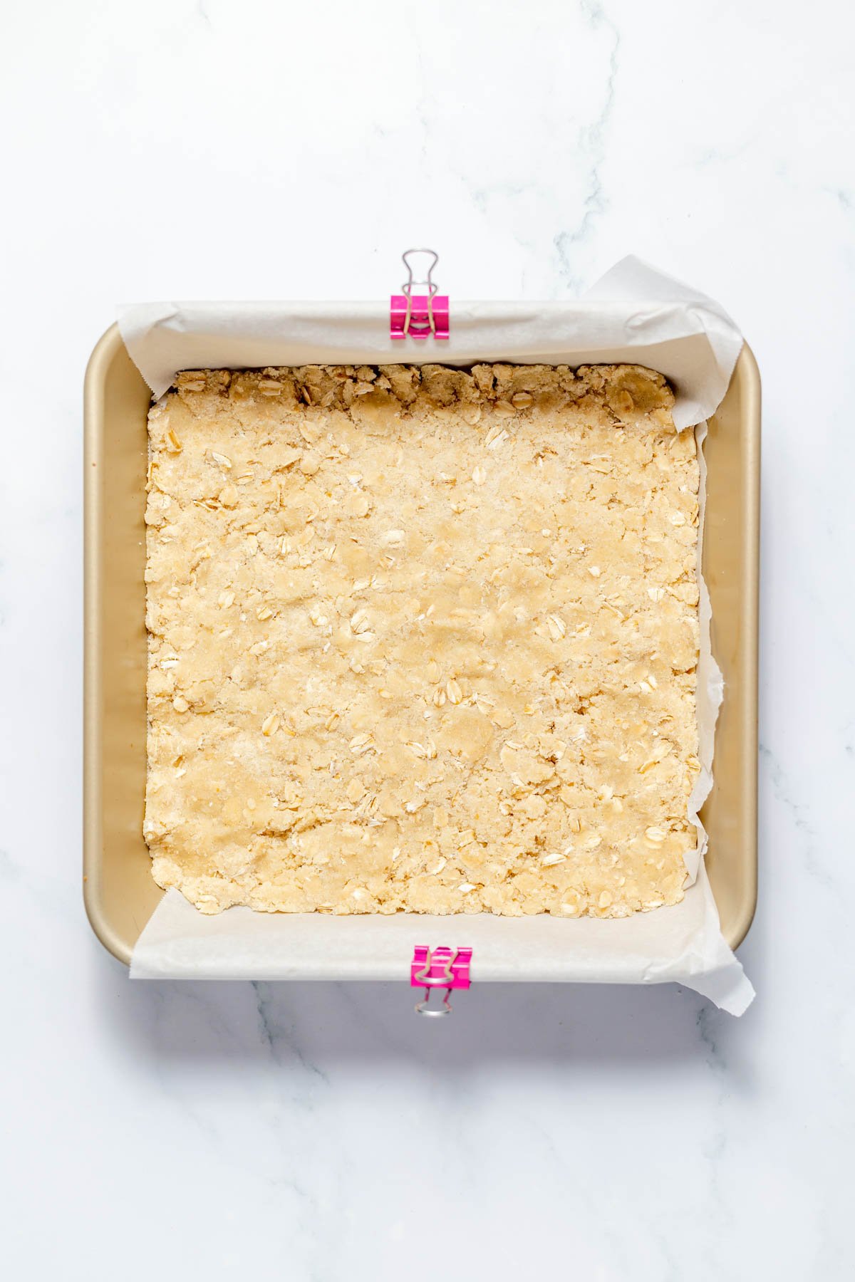 Pressing a portion of the oat crumble mixture into the bottom of a square baking dish.