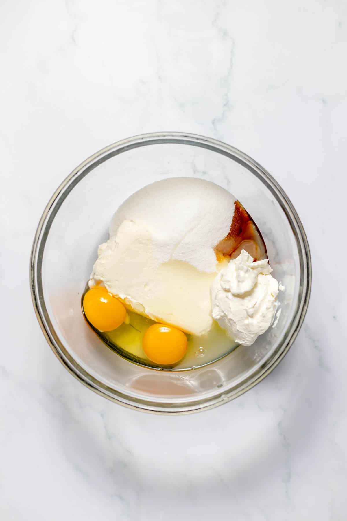 Combining cream cheese, sugar, eggs, vanilla, and sour cream in a glass mixing bowl.