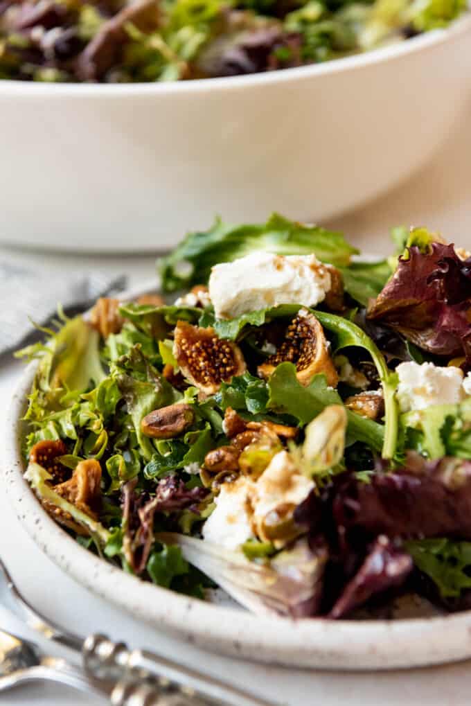 A close image of a serving of salad on a plate with dried figs and goat cheese on top.