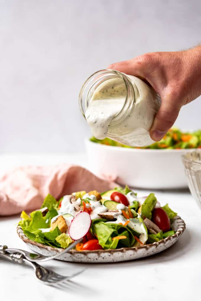 Homemade ranch dressing being poured from a jar onto a crisp green salad.