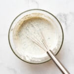 A bowl of homemade ranch dressing with a whisk in it.